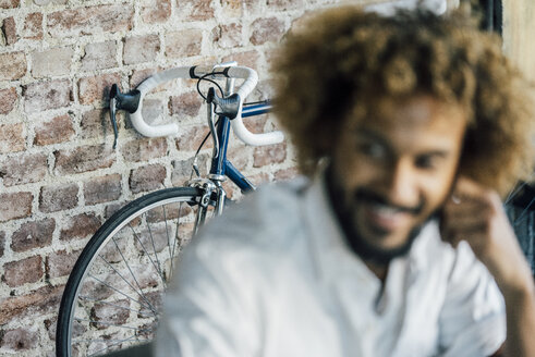 Lächelnder junger Mann mit Fahrrad im Hintergrund - KNSF01734