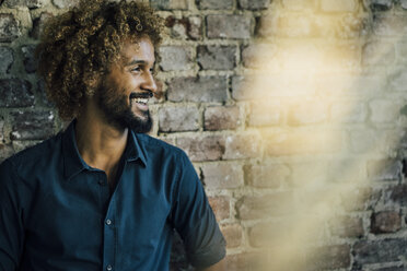 Smiling man with beard and curly hair at brick wall - KNSF01738