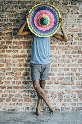 Mann steht an einer Ziegelmauer und bedeckt sein Gesicht mit einem Sombrero, lizenzfreies Stockfoto