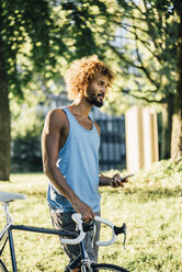 Junger Mann mit Fahrrad und Mobiltelefon im Park - KNSF01746