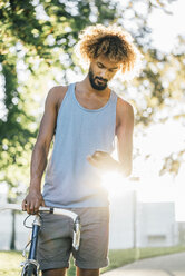 Junger Mann mit Fahrrad, der sein Mobiltelefon überprüft - KNSF01747