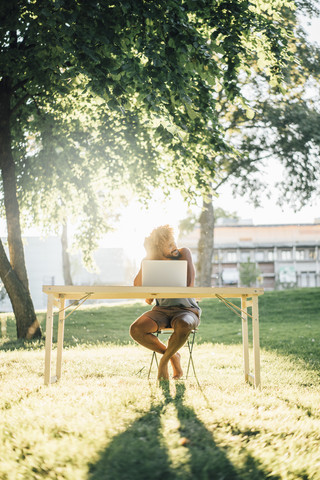 Man with beard and curly hair using laptop at table in park stock photo