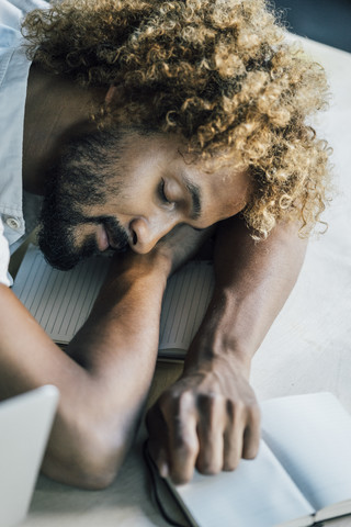 Junger Mann liegt auf dem Schreibtisch und schläft, lizenzfreies Stockfoto