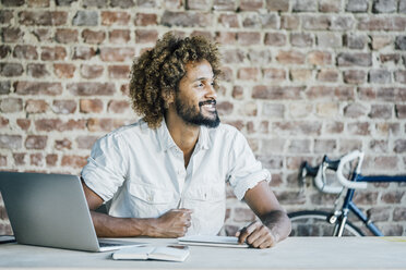 Smiling young man at desk thinking - KNSF01755