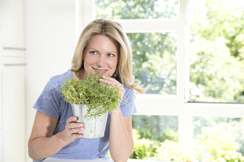 Porträt einer lächelnden Frau mit einem Topf mit Kräutern in der Küche, lizenzfreies Stockfoto