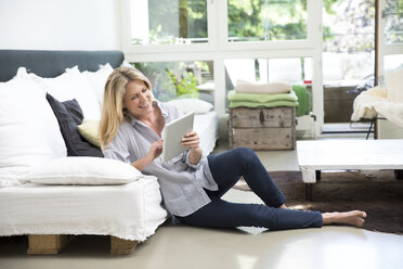 Entspannte Frau sitzt auf dem Boden des Wohnzimmers und benutzt ein Tablet - MAEF12264