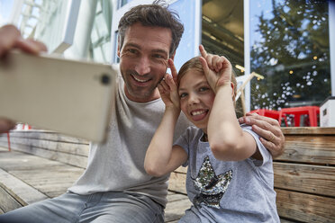 Father and playful daughter taking a selfie at an outdoor cafe - SUF00213