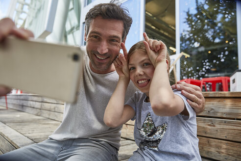 Vater und verspielte Tochter machen ein Selfie in einem Straßencafé - SUF00213