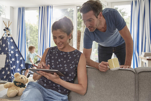 Couple using tablet at home with boy in background - SUF00233