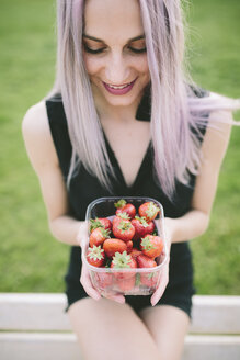 Lächelnde junge Frau, die eine Schachtel mit Erdbeeren hält - GIOF02907