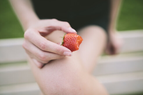 Frauenhand hält angebissene Erdbeere - GIOF02909