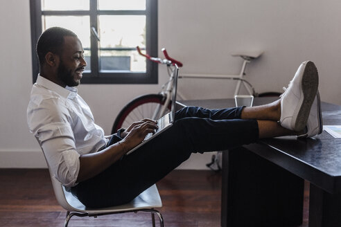 Mann mit Laptop im Heimbüro mit Füßen auf dem Schreibtisch - GIOF02921