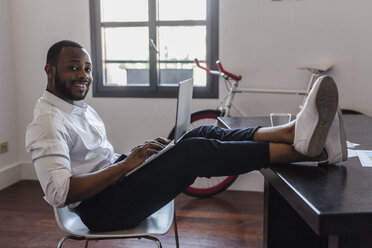 Man using laptop in home office with feet on desk - GIOF02922