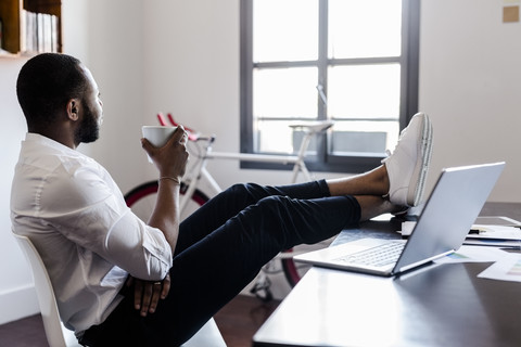 Entspannter Mann im Heimbüro mit Füßen auf dem Schreibtisch, lizenzfreies Stockfoto