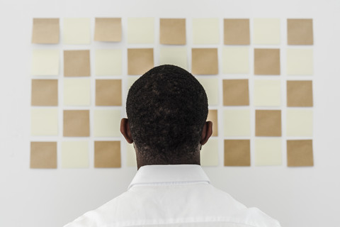 Man looking at adhesive notes on wall in office stock photo