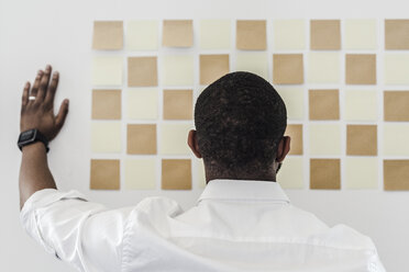 Man looking at adhesive notes on wall in office - GIOF02942