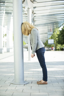 Frustated woman leaning against column - MAEF12269