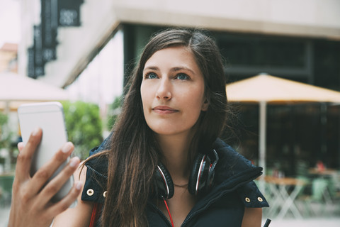 Junge Frau mit Mobiltelefon und Kopfhörern in der Stadt, lizenzfreies Stockfoto