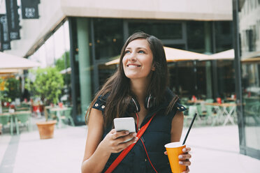 Portrait of smiling young woman with cell phone and takeaway drink in the city - CHAF01910