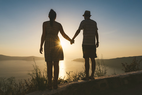 Greece, Santorini, Fira, couple holding hands and enjoying sunset over the Santorini caldera stock photo