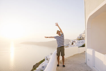 Griechenland, Santorini, Fira, glücklicher Mann im Urlaub mit erhobenen Händen genießt den Sonnenuntergang über dem Meer - GEMF01738
