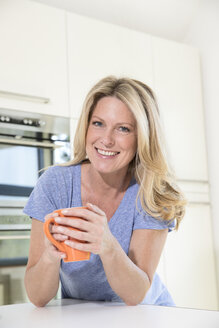 Portrait of smiling woman at home with cup of coffee - MAEF12284