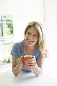 Porträt einer lächelnden Frau zu Hause mit einer Tasse Kaffee - MAEF12286