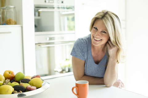 Porträt einer lächelnden Frau zu Hause mit einer Tasse Kaffee und einer Obstschale, lizenzfreies Stockfoto