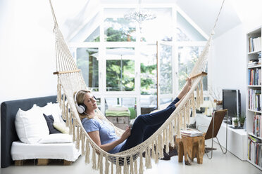 Relaxed woman at home lying in hammock listening to music - MAEF12293