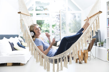 Relaxed woman at home lying in hammock listening to music - MAEF12294