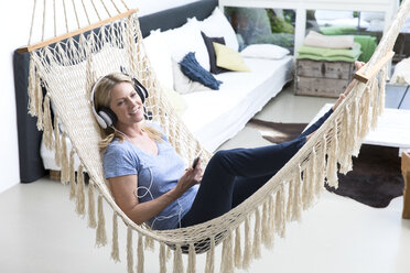 Relaxed woman at home lying in hammock listening to music - MAEF12295