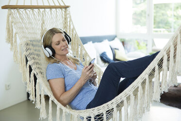Relaxed woman at home lying in hammock listening to music - MAEF12298