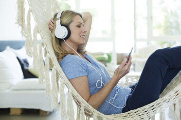 Relaxed woman at home lying in hammock listening to music - MAEF12299