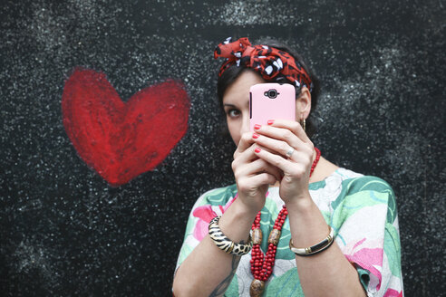 Woman taking a selfie next to heart painted on the wall - RTBF00986