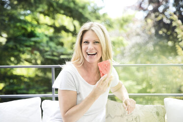 Reife Frau sitzt auf dem Balkon und isst Wassermelone - MAEF12317