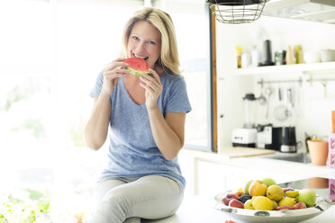 Mature woman sitting in kitchen, eating water melon - MAEF12318