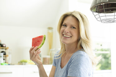 Reife Frau sitzt in der Küche und isst Wassermelone - MAEF12319