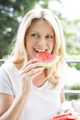 Reife Frau sitzt auf Balkon, isst Wassermelone, Porträt - MAEF12320