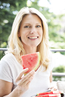 Reife Frau sitzt auf Balkon, isst Wassermelone, Porträt - MAEF12321