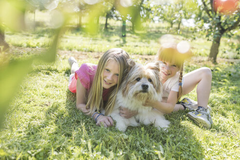 Zwei lächelnde Schwestern liegen mit Hund auf einer Wiese - SHKF00761