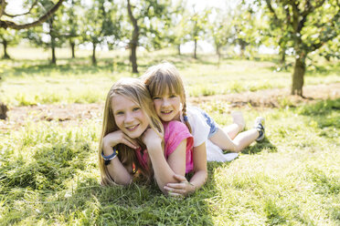 Two smiling sisters lying on meadow - SHKF00775