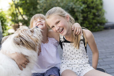 Zwei glückliche Schwestern kuscheln mit dem Hund im Garten - SHKF00783