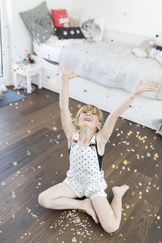 Mädchen zu Hause sitzt auf dem Boden und wirft Konfetti, lizenzfreies Stockfoto