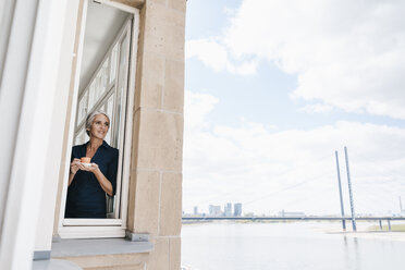 Geschäftsfrau schaut aus dem Fenster in einem Büro am Wasser - KNSF01768