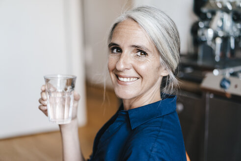Portrait of smiling businesswoman holding glass of water - KNSF01773