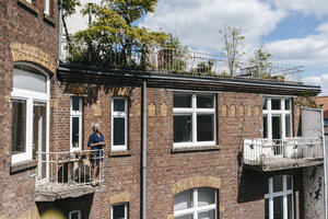 Frau steht auf dem Balkon eines Backsteinhauses - KNSF01775