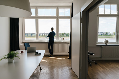 Geschäftsfrau steht in einem modernen Büro und schaut aus dem Fenster, lizenzfreies Stockfoto