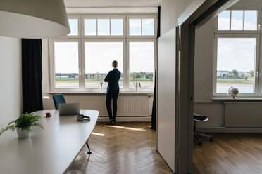 Geschäftsfrau steht in einem modernen Büro und schaut aus dem Fenster - KNSF01777