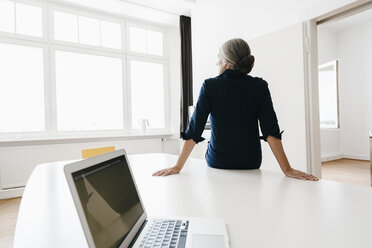 Geschäftsfrau sitzt auf einem Tisch in einem modernen Büro - KNSF01806