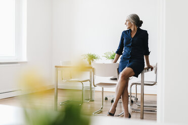 Businesswoman sitting on table in modern office - KNSF01810